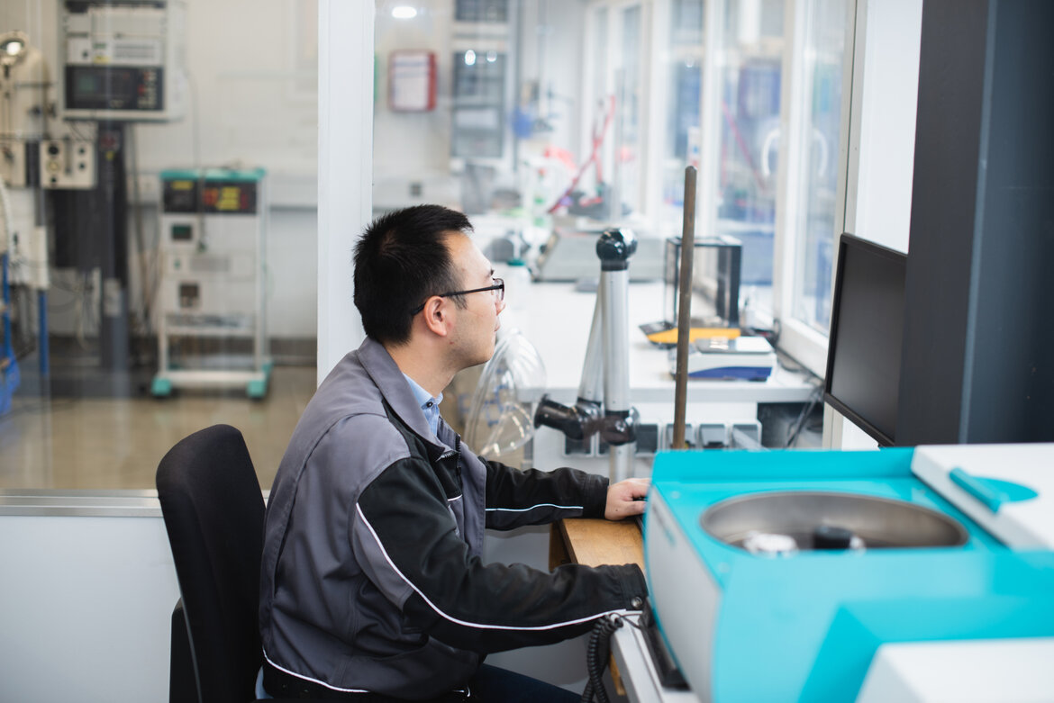 Ein Mann sitzt in einer Laborumgebung an einem Schreibtisch und sieht zum Monitor