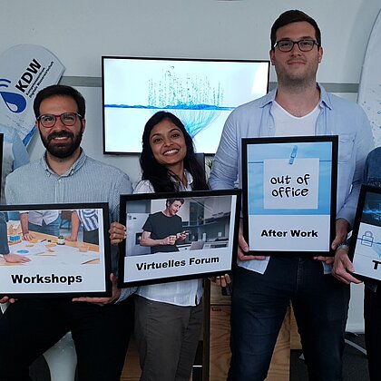 Teilnehmende eines Workshops präsentieren die Schilder „Early Bird“, „Wokshops“, „Virtuelles Forum“, „After Work“ und „Thementage“