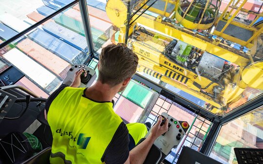 Mann blickt aus einem Hafenkran auf die Container