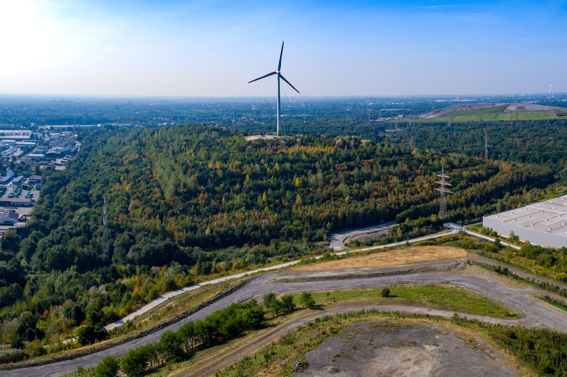 Luftbild der Abraumhalde mit Windrad vor blauem Himmel