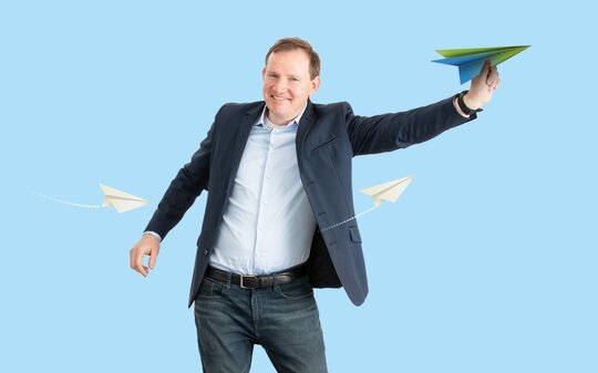 Mann im Anzug, der in der Hand eine Papierschwalbe hält, das Logo des Umweltwirtschaftspreis.NRW