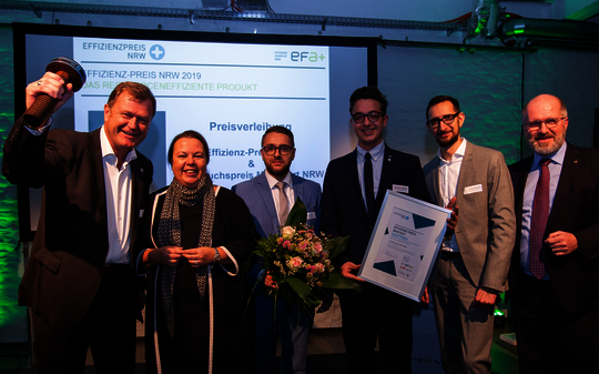 Im Beisein der Ministerin jubelt das Gewinnerteam des Effizienzpreis-NRW und streckt die Auszeichnung in die Höhe