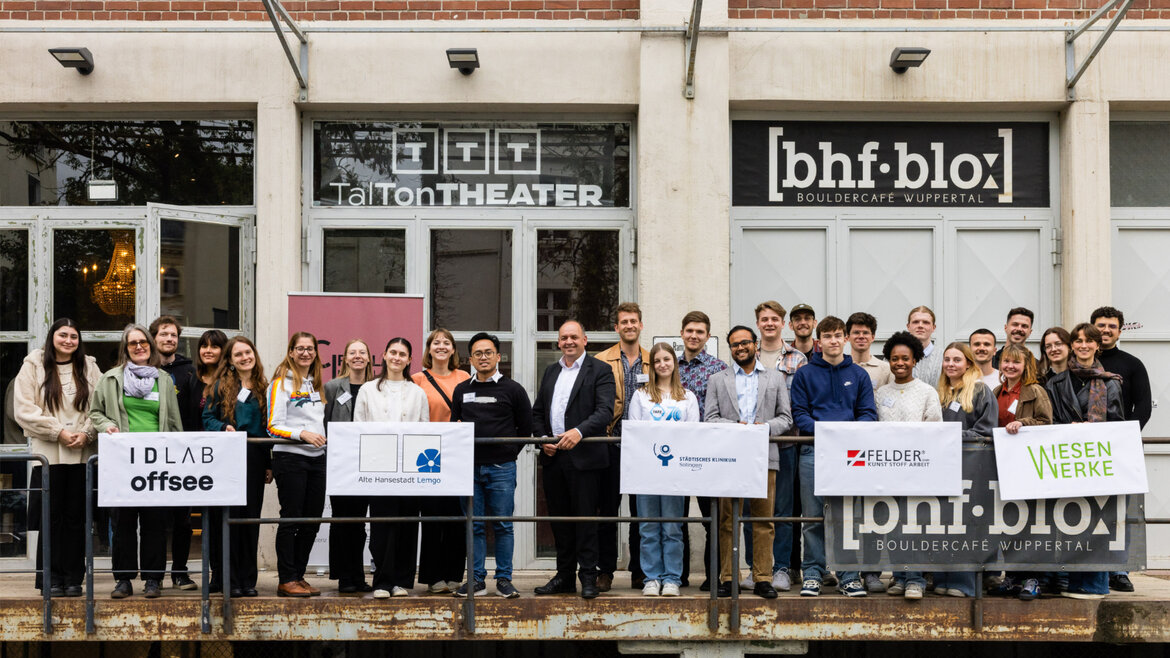 Gruppenfoto der Teilnehmenden vor dem Veranstaltungsraum, die Gruppen zeigen jeweils das Logo des Casegebers