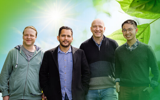 Gruppenbild: Vier Herren, im Hintergrund die Sonne und ein grünes Blatt
