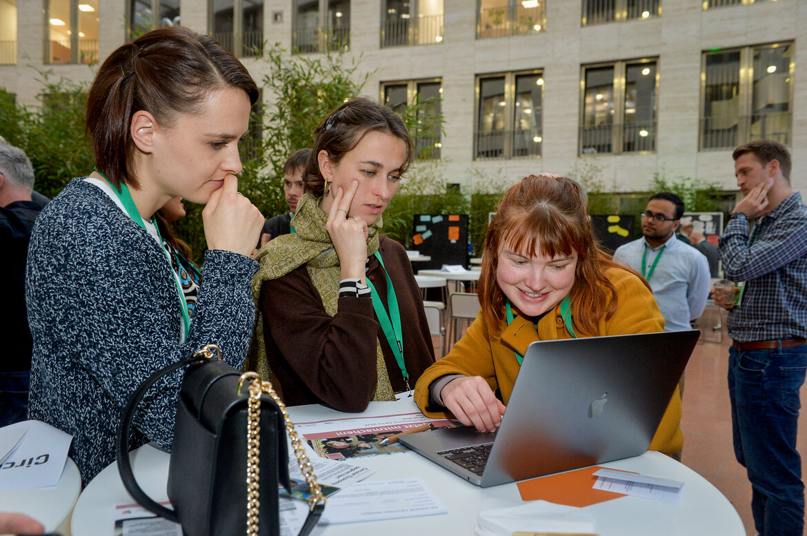 Bei der Ausstellung: Eine Gruppe von Frauen betrachtet etwas auf einem Laptop 