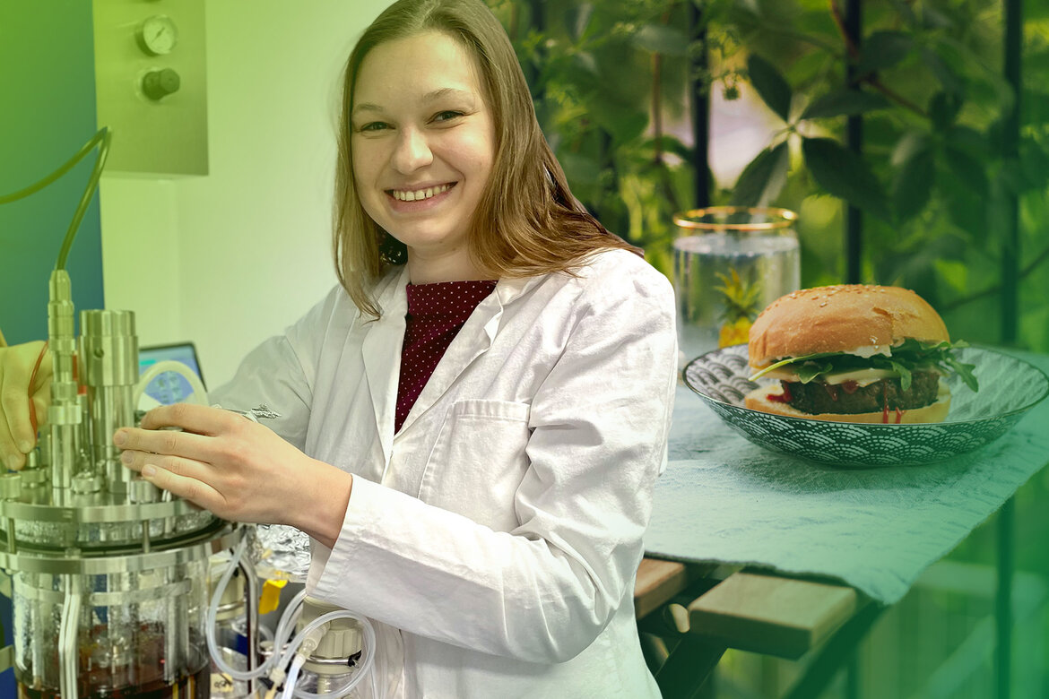 Eine Frau steht an einem Laborgerät, im Hintergrund ein Burger auf einer Servierschale