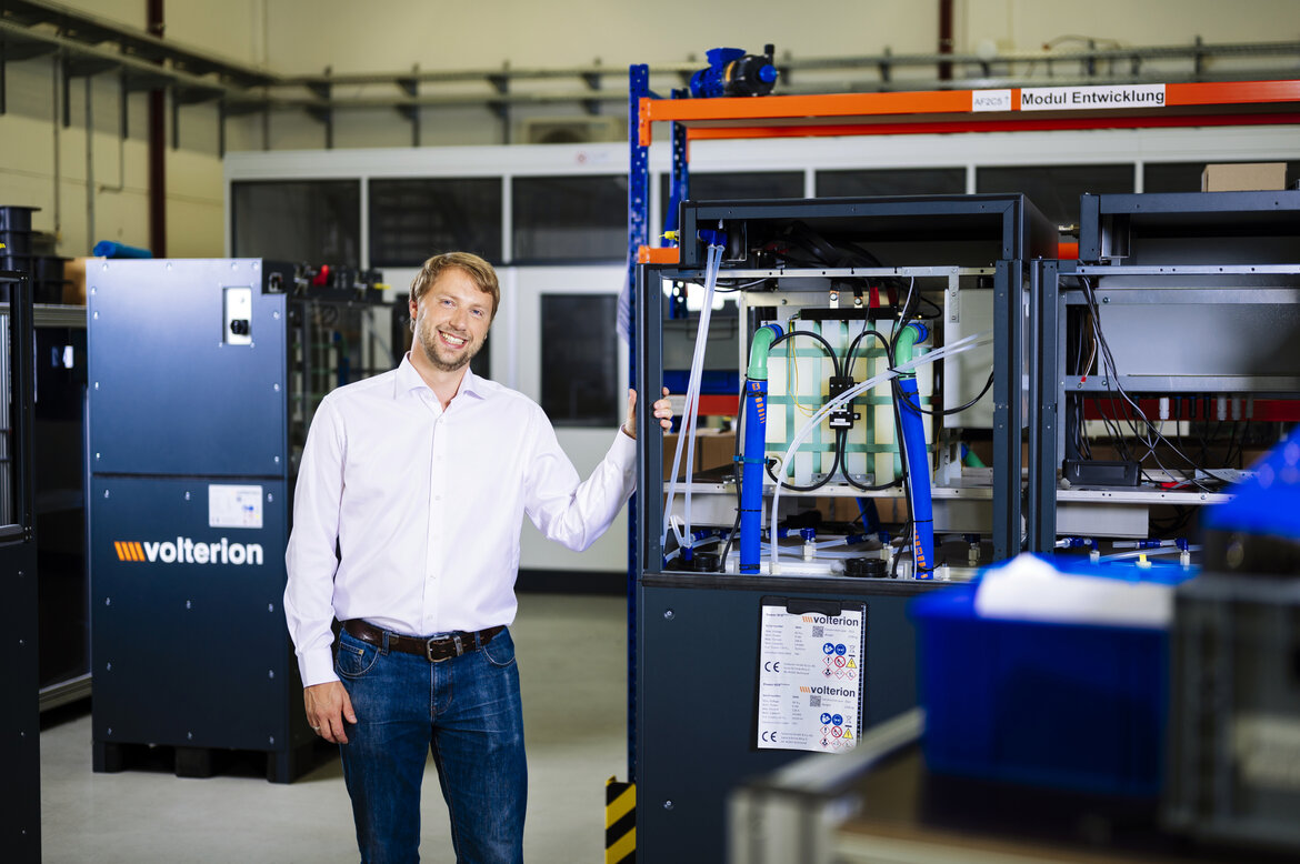 Ein junger Mann vor einer großen Batteriekonstruktion aus Metall und Kunststoff