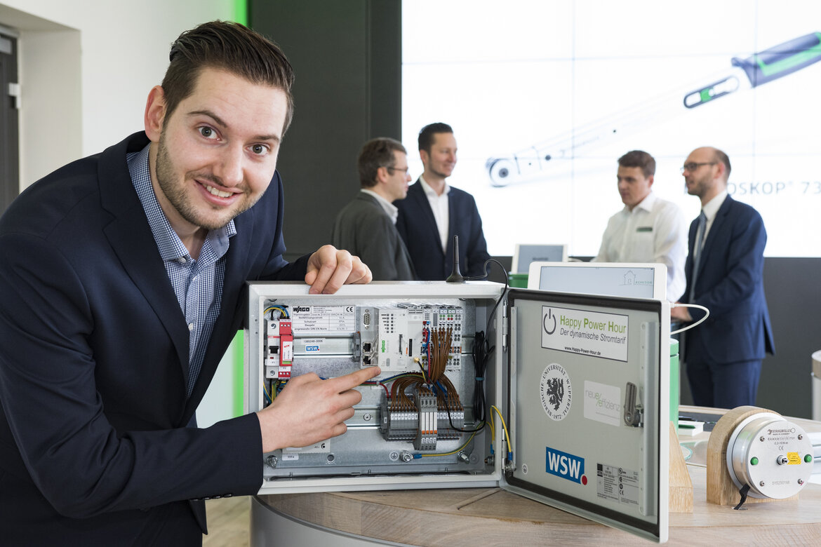 Ein junger Mann zeigt auf einen geöffneten Schaltkasten mit einem Smart Meter