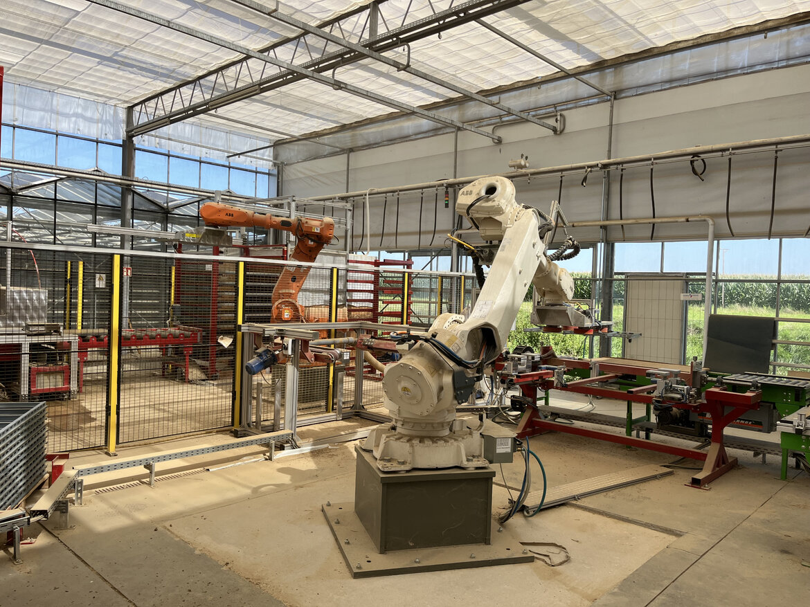 In einem Glashaus arbeitet ein Industrieroboter mit Lehmbauplatten