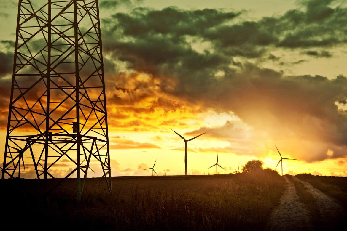 Windräder und ein Strommast im Sonnenuntergang