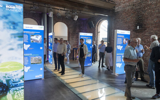 Veranstaltungsgäste betrachten beleuchtete Ausstellungstafeln mit den Projekten der Greentech.Ruhr
