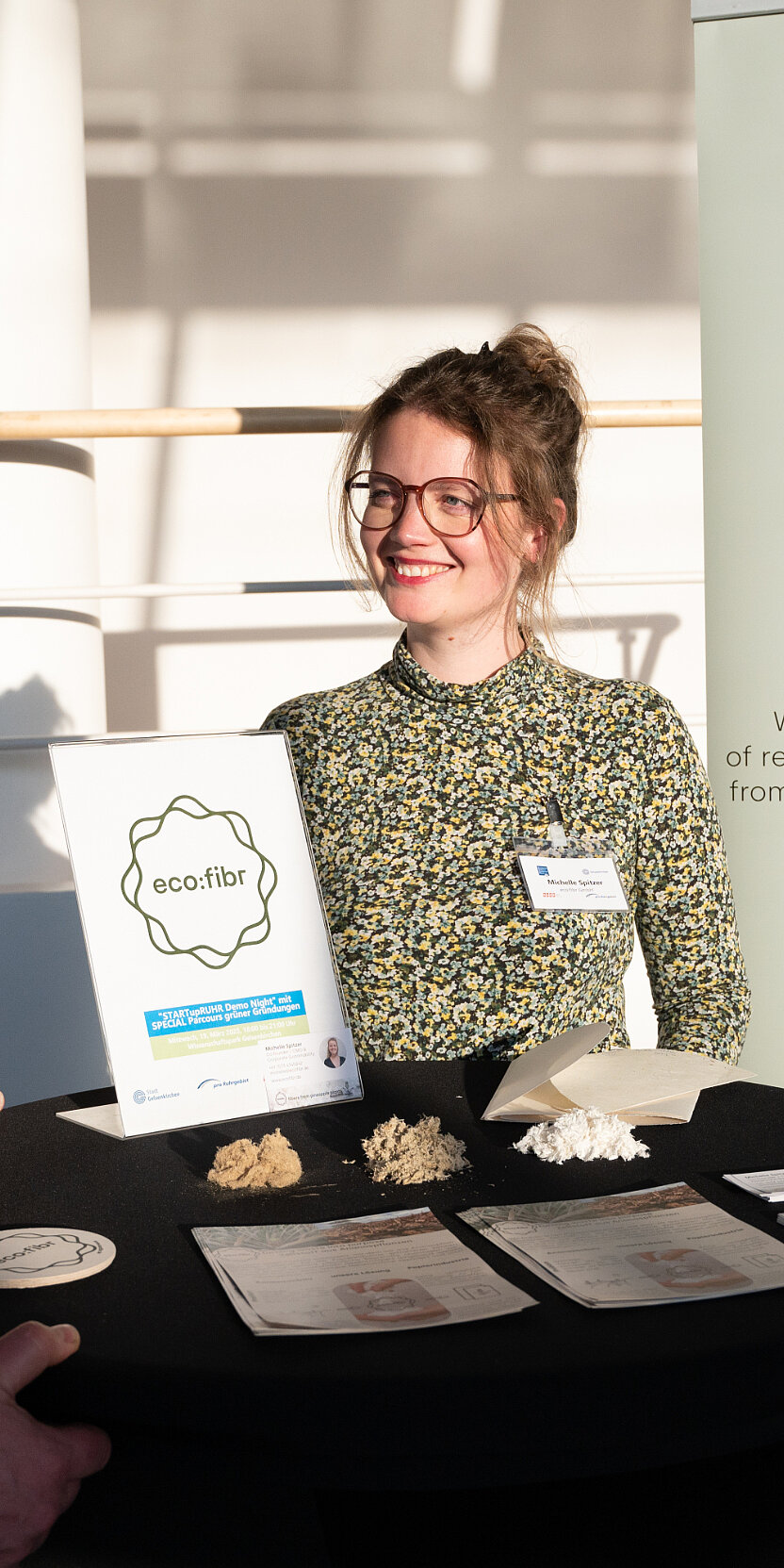 Eine junge Frau präsentiert an einem Ausstellungsplatz ressourcenschonende Planzenfasern
