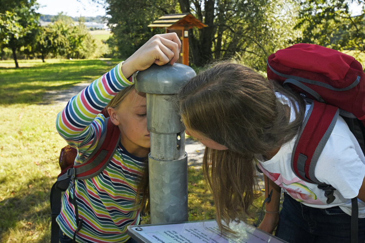 Kinder trinken an einem Rohr auf einer Streuobstwiese