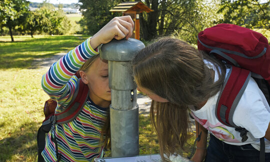 Kinder trinken an einem Rohr auf einer Streuobstwiese