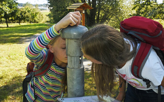 Kinder trinken an einem Rohr auf einer Streuobstwiese