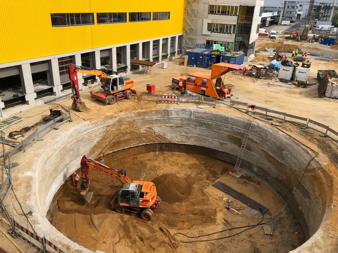 Auf einer Baustelle wird ein kreisrundes Loch ausgehoben, ein Bagger steht darin