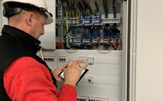 Mann mit Helm vor einem Schaltschrank