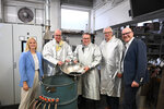 Gruppenbild in Schutzkleidung: Minister Oliver Krischer und vier weitere Personen an einer Maschine, in der Hand ein Metallbehälter