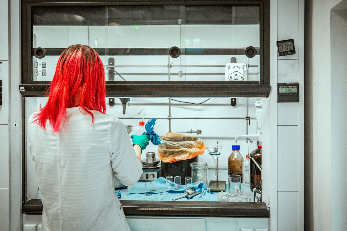 Eine Frau mit roten Haaren sitzt im Labor an einem Abzug