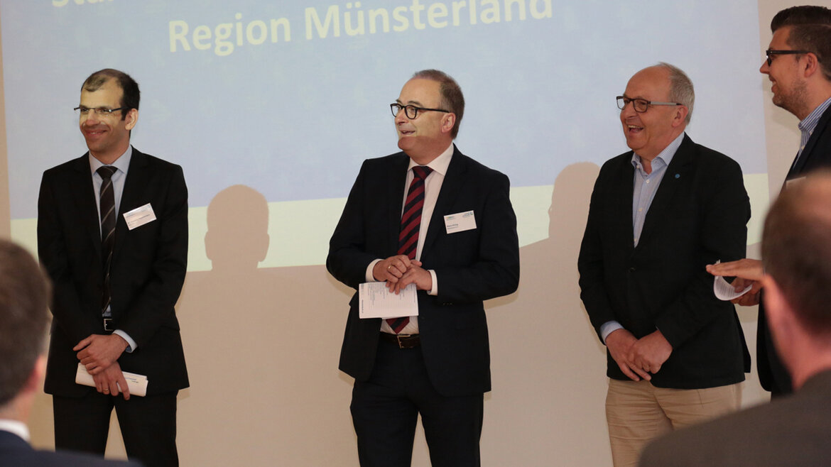 Die vier Herren stehen vor einer Beamerprojektion.