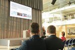 Durch das Publikum fotografiert sieht man den Redner auf dem Podium