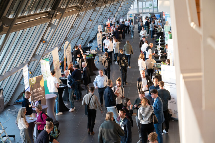 Infostände und Besucherinnen und Besucher unter dem hellen Glasdach des Wissenschaftsparks