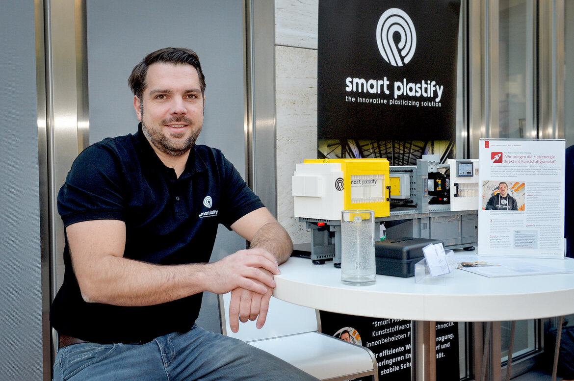 Ein Mann sitzt an einem Tisch auf dem verschiedene technische Geräte stehen, um sein Projekt smart plastify vorzustellen