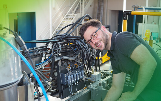 Ein junger Mann beugt sich über eine komplizierte Maschine zur Kunststoffverarbeitung
