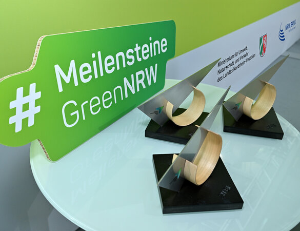 Drei Trophäen und der Schriftzug #MeilensteineGreenNRW