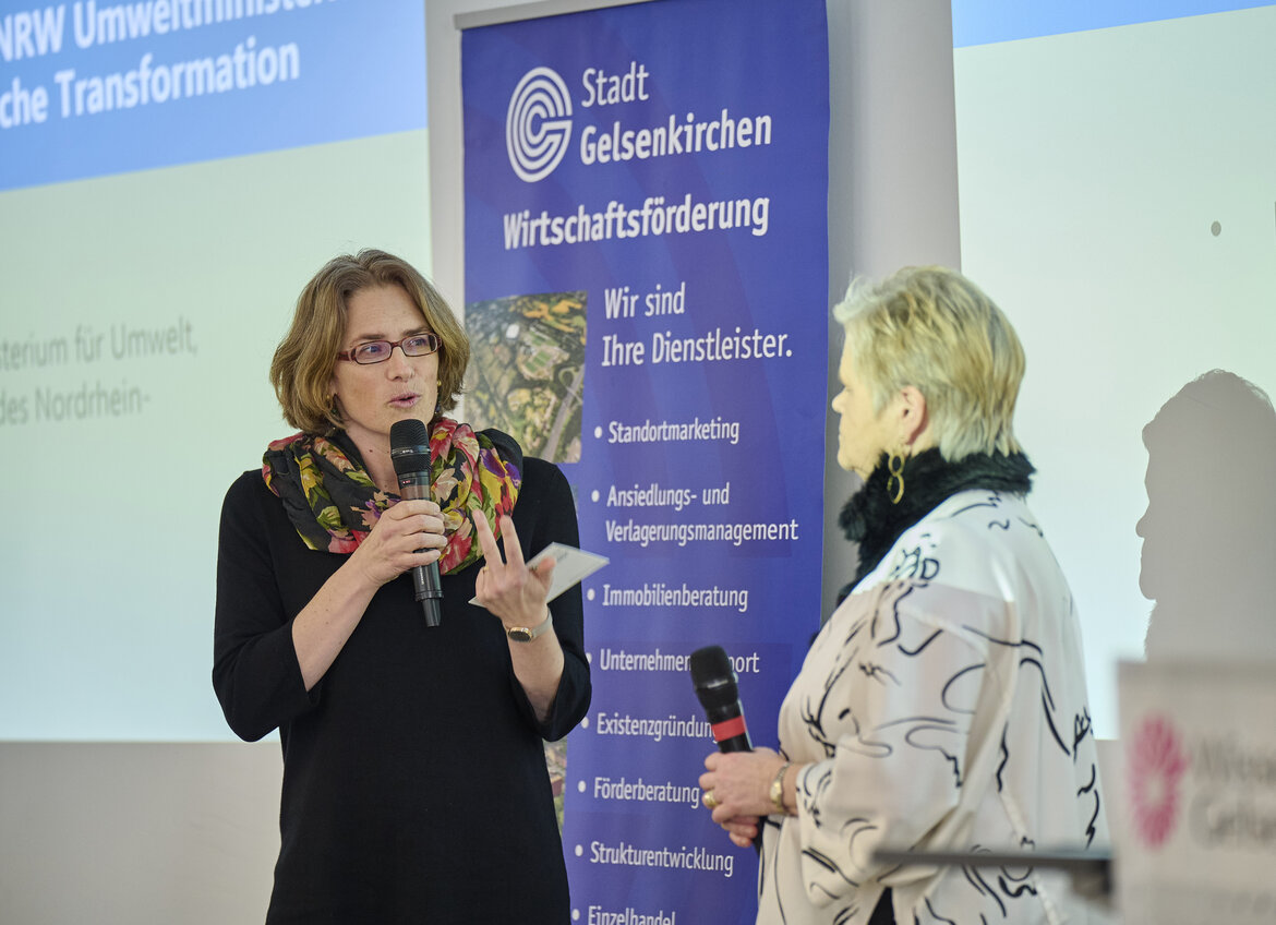 Lara Wever und Dr. Ute Günther mit Mikrofonen in der Hand, im Hintergrund eine Beamerprojektion