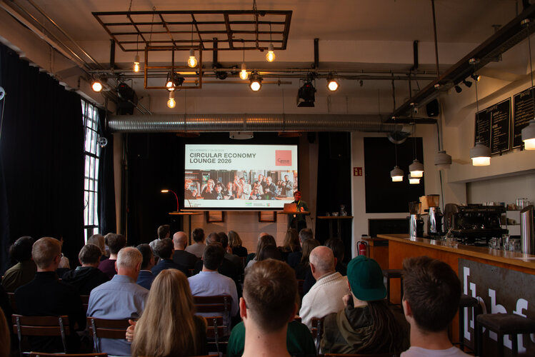 Eine Rednerin zeigt die Folie Circular Economy Lounge 2026 in einem gut besetzten Saal